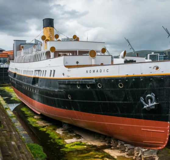 Restored historic ship, SS Nomadic, docked in a shipyard under a cloudy sky.